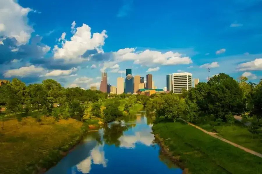 Houston: A Safe and Comfortable Destination for High-End Travelers. The image depicts green trees surrounding a body of water under a blue sky during the daytime.